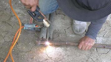 un soldador está trabajando en la soldadura de acero. uniforme, máscara de soldadura y pieles de soldadores, metal de soldadura con una máquina de soldadura por arco en el sitio de construcción, chispas azules vuelan a los lados video