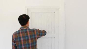 A painter is painting white with a painted plot on the door of a white wooden house.