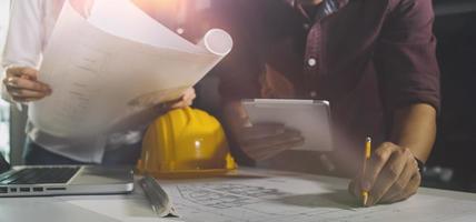 Two colleagues discussing data working and tablet, laptop with on on architectural project at construction site at desk in office photo