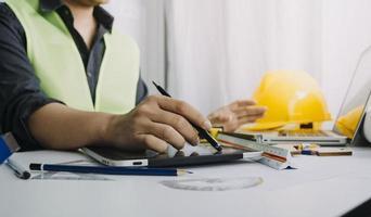 Two colleagues discussing data working and tablet, laptop with on on architectural project at construction site at desk in office photo