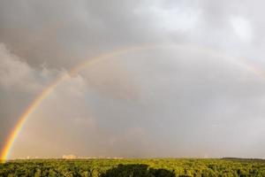 large rainbow in gray blue sky over sunlit park photo