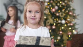 Two young girls laugh and play with wrapped gifts in front of a decorated tree video