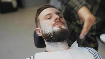 le coiffeur applique de la crème à raser sur le cou et le visage du client incliné video