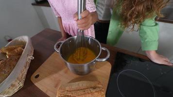 Young woman and girl use a big whisk to stir ingredients in a pot video