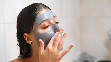 Young woman with wet hair applies clay mask to face video