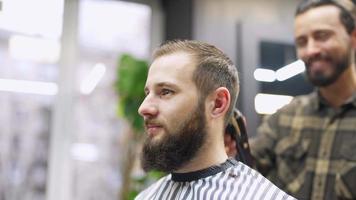 coiffeur coupe les cheveux d'un client masculin avec un peigne et une tondeuse video