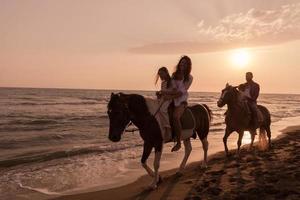 The family spends time with their children while riding horses together on a sandy beach. Selective focus photo