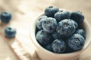 Freshly picked juicy blueberries in the bowl on wooden background, close up. Blueberries background. photo