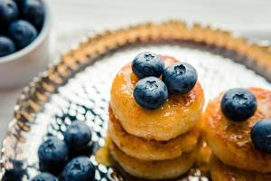 Homemade cheesecake with freshly picked juicy blueberries in the plate on wooden background, close up photo