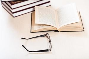 spectacles and open book near stack of books photo