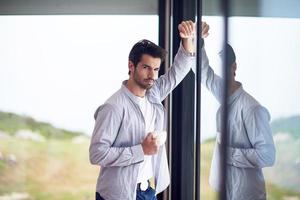 relaxed young man drink first morning coffee withh rain drops on window photo