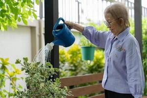 mujer mayor con pérdida de cabello después de la quimioterapia por cáncer de mama regando plantas en el jardín foto