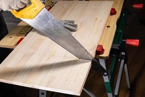 side view of sawing wooden board with hand saw photo