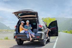 Group of of friend sitting in open trunk of a black car looking at tablet. photo