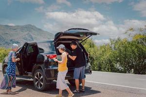 hombre con amigos cargando equipaje en el maletero del automóvil, viajando en vacaciones de verano. foto