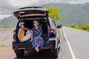 Two woman sitting at the car trunk on a road trip.