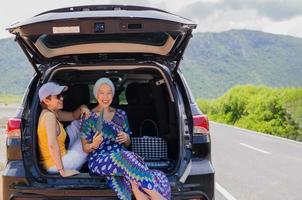 Two happy woman sitting at the car trunk on a road trip. photo