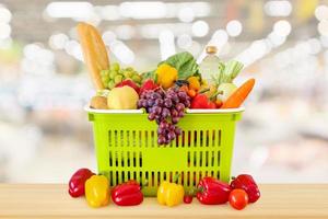 cesta de la compra llena de frutas y verduras en la mesa de madera con fondo desenfocado borroso de la tienda de comestibles del supermercado foto
