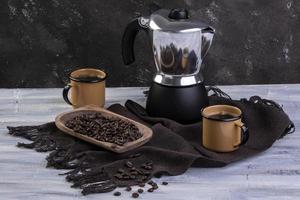 cafetera italiana y dos tazas de café con granos de café tostados en un recipiente de madera