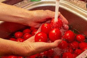 The woman's hands wash the tomatoes and remove the stalks from the vegetables. photo