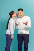 Portrait of a happy young couple standing together over blue background, telling secrets photo