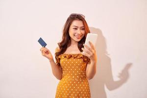 retrato de una niña feliz sosteniendo un teléfono móvil y una tarjeta de crédito aislada sobre el fondo de biege foto