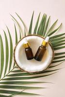 Coconut oil in bottle with open nuts and pulp in jar, green palm leaf background. Natural cosmetic products. photo