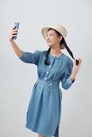 Happy beautiful girl in casual or hipster style, pigtail hairstyle, standing, holding mobile smart phone and doing selfie photo