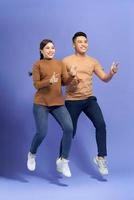 Energetic beautiful couple posing together on camera while running or jumping and pointing fingers on copyspace along background