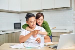 feliz pareja joven esposo y esposa usando una computadora portátil mirando la pantalla pagar facturas en línea en la aplicación calcular el pago de la inversión hipotecaria foto