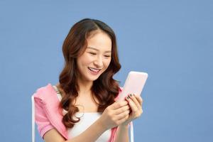 Happy young Asian woman texting message with her smartphone isolated blue background.