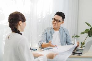 Dos colegas discutiendo el trabajo de datos y una tableta, un portátil con un proyecto arquitectónico en el sitio de construcción en un escritorio en la oficina foto