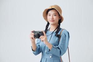Young cheerful female tourist photographer is excited and holding camera, wearing hat on white background photo