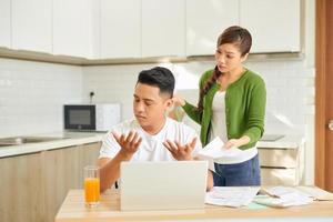 Angry young couple shouting in a hard quarrel by their many debts at home. Financial family problems concept. photo