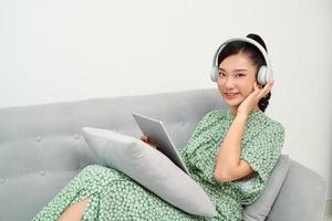 chica escuchando música en línea con una tableta sentada en un sofá en la sala de estar en casa foto