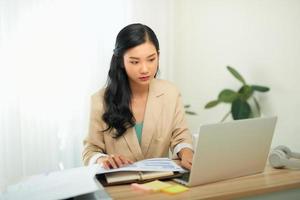 Beautiful young woman in casual clothing using laptop and smiling while working indoors photo