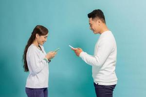 Face-to-face conversation. Excited man and woman talking holding smartphones looking at each other standing over blue background. photo