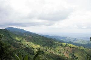 Rural mountain view with cloudy sky and hilly jungle. Green hilltop view with a drone. Hiking trail landscape photograph of hills. Beautiful hill station photo at Bandarban, Bangladesh.