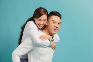 Piggyback ride. Young man carrying girlfriend on his back, blue background with copy space. photo