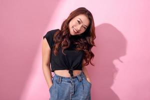 hermoso retrato asiático jovencita alegre posando con ropa informal con una sonrisa radiante de pie aislada en un fondo rosa foto