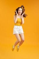 Joyful young asian girl having fun fooling around jumping doing winner gesture on yellow background. photo