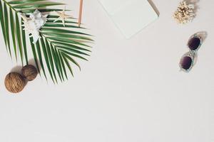 Flat lay beach accessories sunglasses, diary, coconuts with palm branches and shells photo