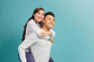 Love forever, fun together. Young handsome boyfriend is piggybacking his cute lover, on blue background photo