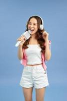 Beautiful Asian woman singing karaoke isolated over blue background. photo