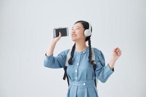 Carefree happy asian woman in headphones, playing karaoke app on mobile phone photo