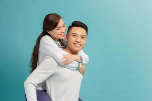 Image of lovely couple having fun while man piggybacking his girlfriend isolated over blue background photo