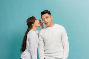 Portrait of a happy young couple standing together over blue background, telling secrets photo