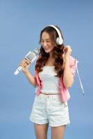 Young Asian woman listening to music with headphones, singing song in microphone over blue background. photo