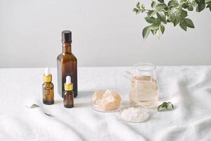 Aromatherapy. Small glass bottles with cosmetic oils. Bath salt. Fresh leaf. Objects for spa procedures on white background oil, leaf. photo