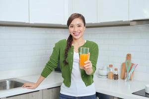 Portrait of a smiling young woman drinking orange juice in the kitchen at home photo